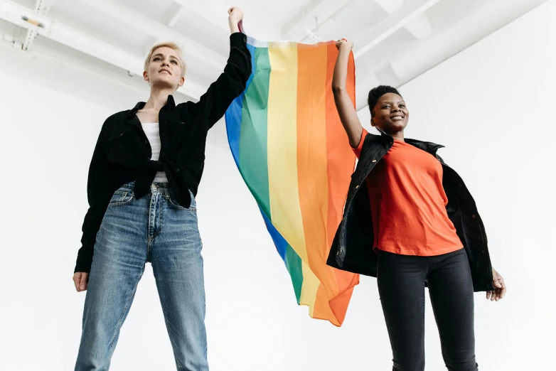 two people standing next to each other holding a rainbow flag, trending on unsplash, hands in air, woman holding another woman, androgyny, with a white background