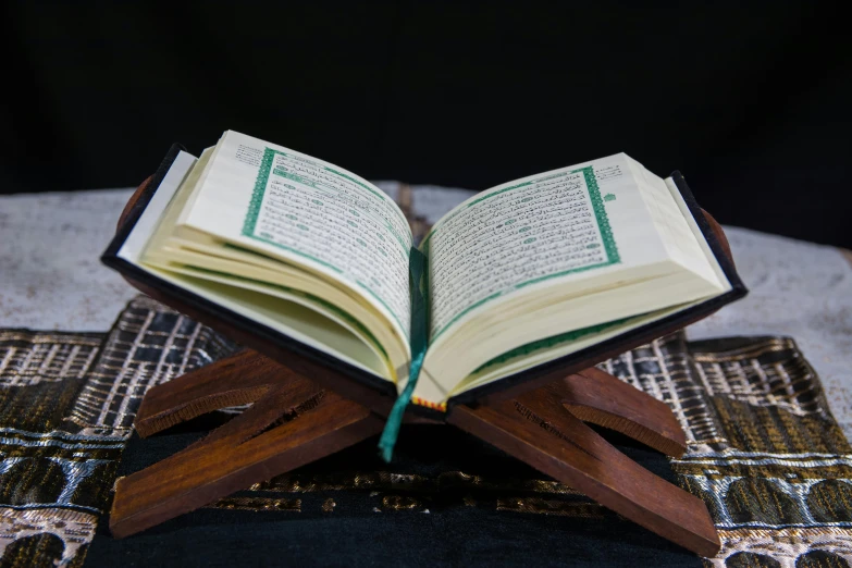 an open book sitting on top of a wooden stand, hurufiyya, professionally assembled, riyahd cassiem, beautifully lit, black