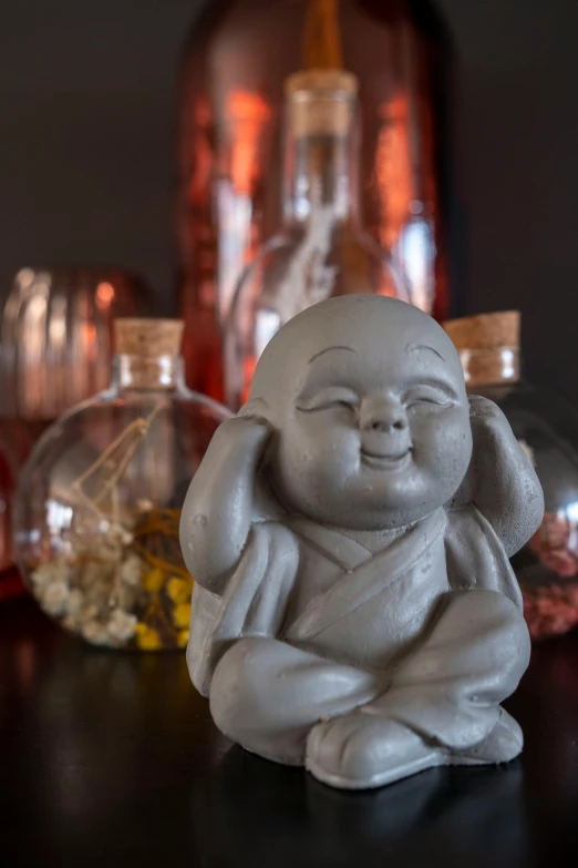 a buddha figurine sitting on top of a table, inspired by Jin Nong, concrete art, playful smirk, a close up shot, jar on a shelf, fisting monk