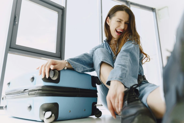 a woman sitting on the floor next to a blue suitcase, pexels contest winner, happening, laughing maniacally, avatar image, closeup - view, luggage