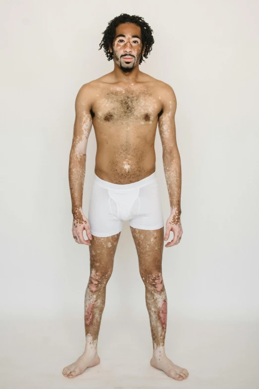 a man covered in mud standing in front of a white wall, by Ellen Gallagher, wearing white tights, white fluffy cotton shorts, anatomically correct body, riyahd cassiem