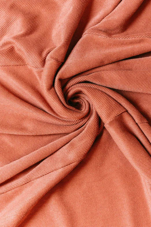 a close up image of an orange fabric, corduroy road, faded pink, spiralling, bottom body close up