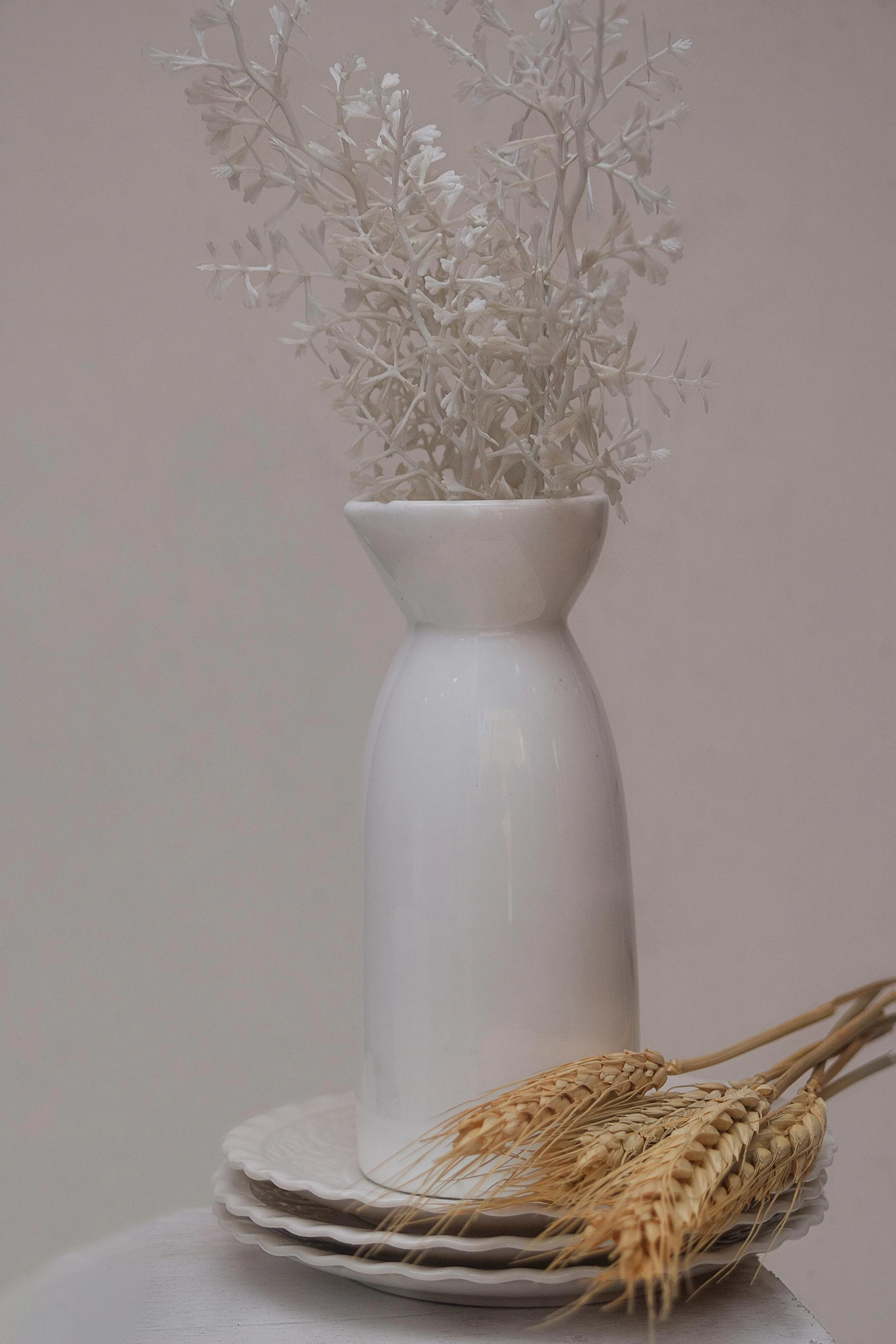 a white vase sitting on top of a stack of plates, made of dried flowers, detailed product image, background image, small details