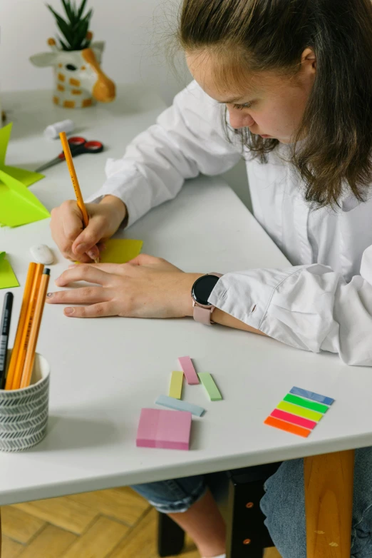 a woman sitting at a table writing on a piece of paper, arbeitsrat für kunst, with fluo colored details, origami, thumbnail, avatar image