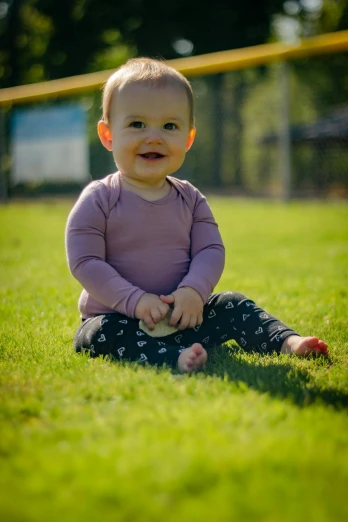 a baby sitting on top of a lush green field, on a soccer field, purple, baseball, portrait image