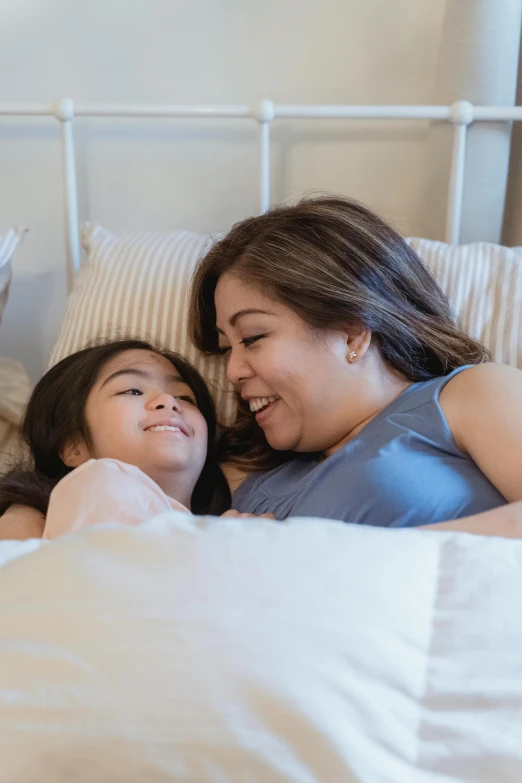 a couple of women laying in bed next to each other, pexels contest winner, incoherents, happy kid, manila, daughter, smiling at each other
