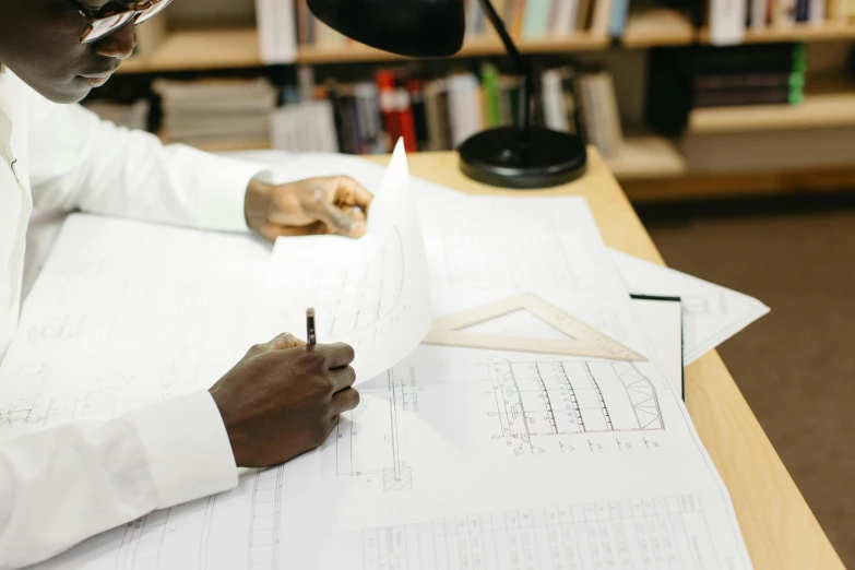 a man sitting at a desk writing on a piece of paper, a drawing, reading engineering book, white map library, high-quality photo, riyahd cassiem