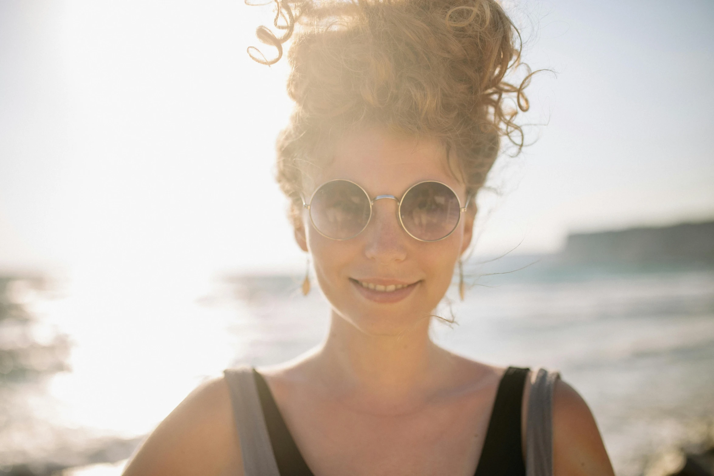 a woman standing on top of a beach next to the ocean, pexels contest winner, renaissance, curly messy high bun hairstyle, in sun glasses, closeup headshot, avatar image