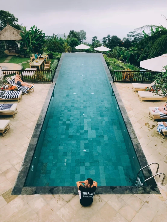 a man sitting on the edge of a swimming pool, lush vista, flatlay, bali, repeating