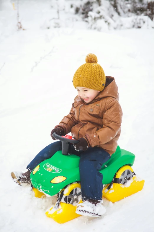 a young boy sitting on a green sled in the snow, pexels, process art, driving in a little toy car, yellow, square, high quality photo