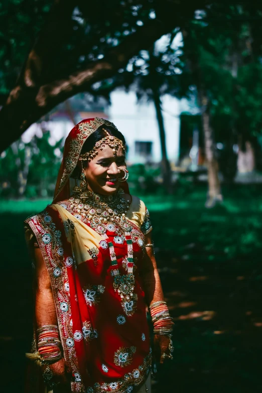 a woman in a red and gold outfit standing under a tree, inspired by Steve McCurry, pexels contest winner, renaissance, bride, madly grinning, sri lanka, a still of a happy