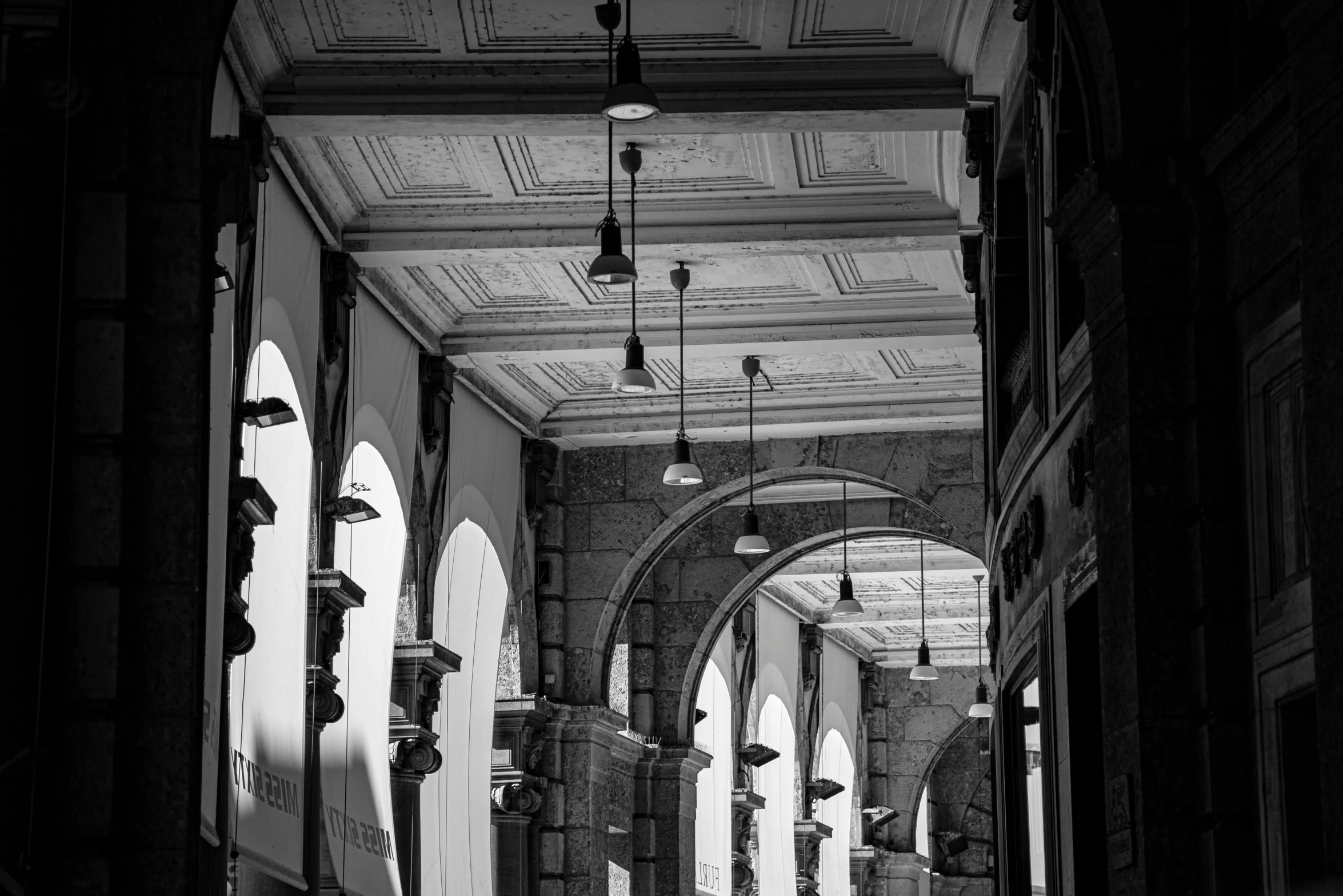 a black and white photo of the inside of a building, by Kristian Kreković, pexels contest winner, blue lamps on the ceiling, white stone arches, palermo city street, nice afternoon lighting