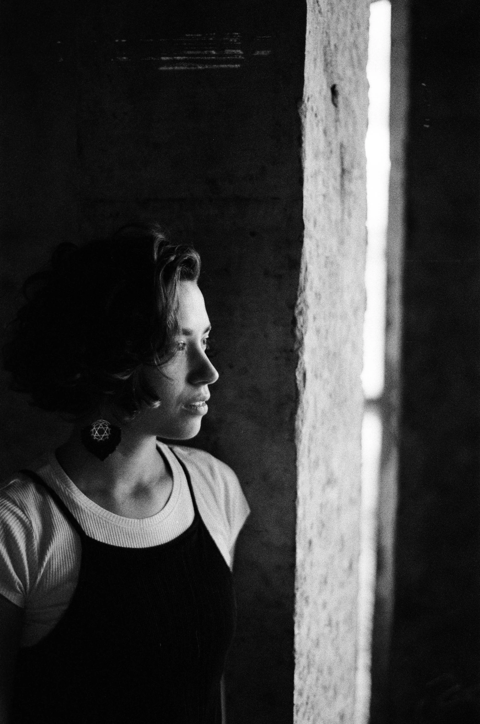 a black and white photo of a woman looking out a window, oona chaplin, tri-x 400 side lighting, in a castle, frida castelli