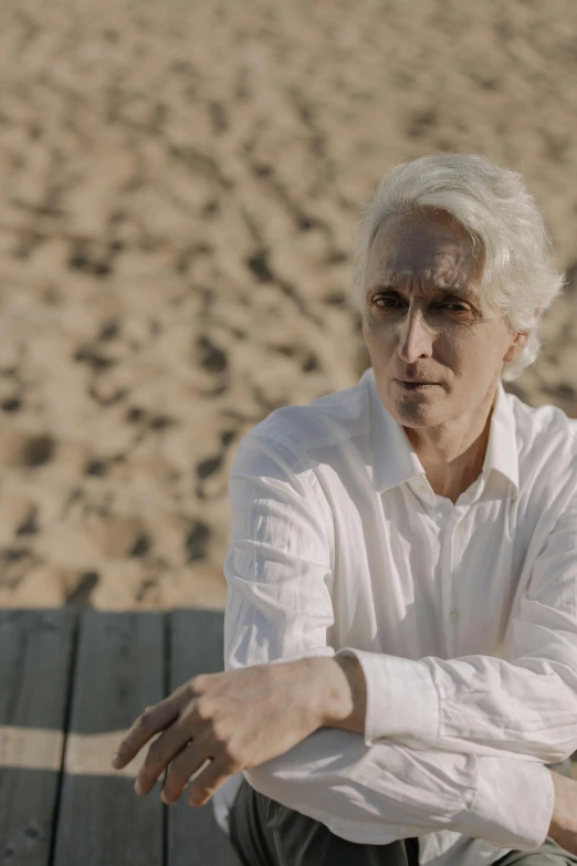 a man sitting on top of a wooden bench, an album cover, inspired by Murray Tinkelman, unsplash, romanticism, intense white hair, on beach, still image from tv series, androgynous person