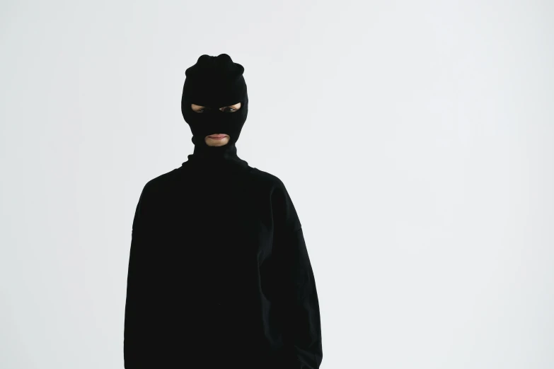 a man wearing a cat mask standing in front of a white background, an album cover, inspired by Zhu Da, unsplash, antipodeans, dressed black hoodie, female thief, dezeen, burka