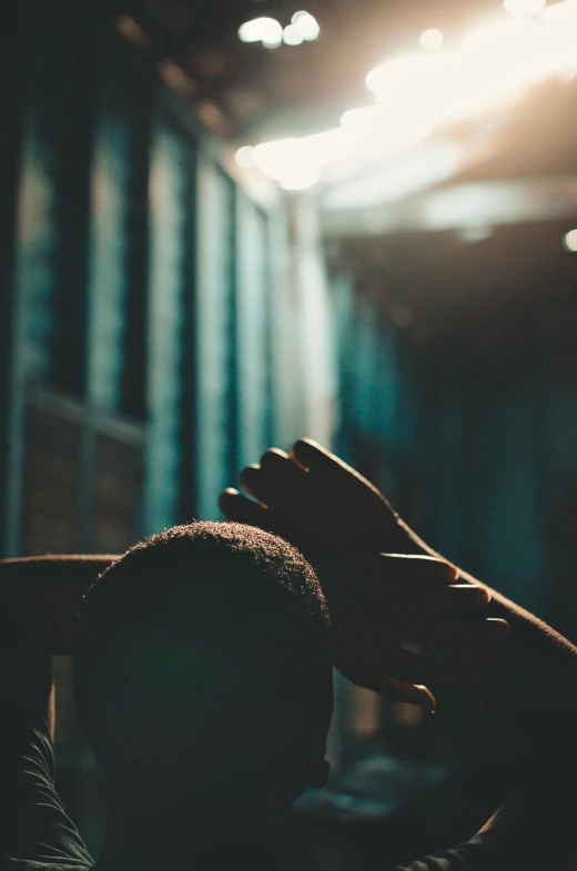 a man sitting in front of a window with his hands on his head, inspired by Elsa Bleda, pexels contest winner, in a dark warehouse, prayer hands, black man, behind bars