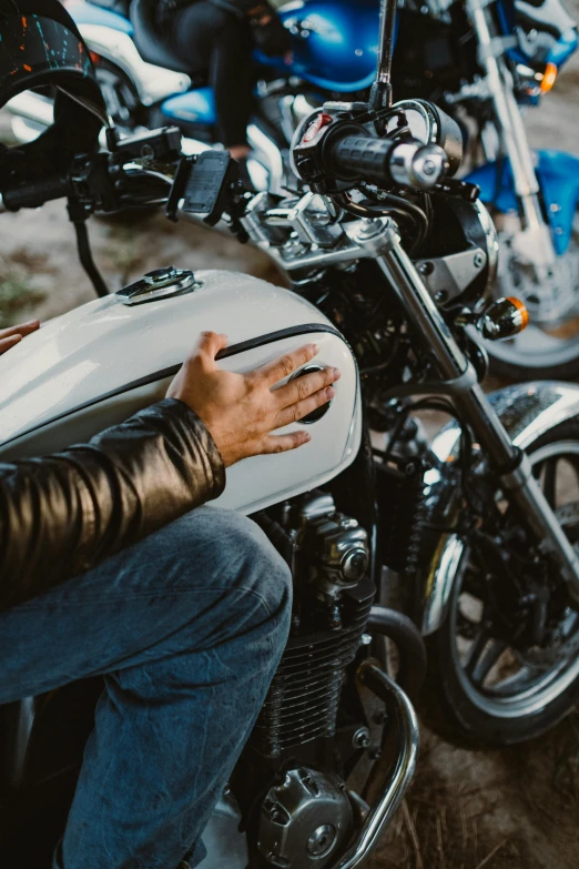 a man in a leather jacket sitting on a motorcycle, a photo, trending on pexels, hands shielding face, white metallic, white mechanical details, touring