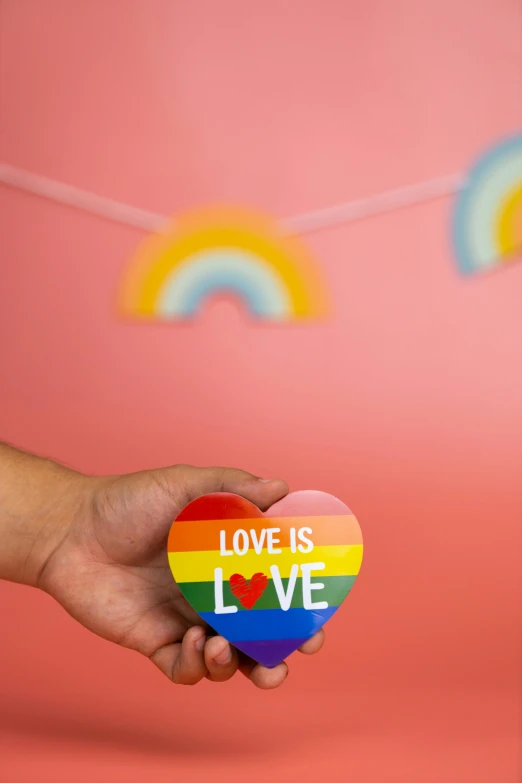 a person holding a heart with the word love is love on it, inspired by Okuda Gensō, trending on pexels, emma bridgewater and paperchase, product display photograph, made of glazed, badge