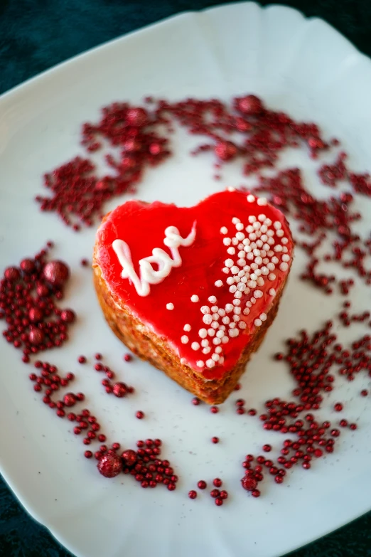 a heart shaped cake on a plate with sprinkles, a photo, by Julia Pishtar, romanticism, reddish, bo chen, close, back