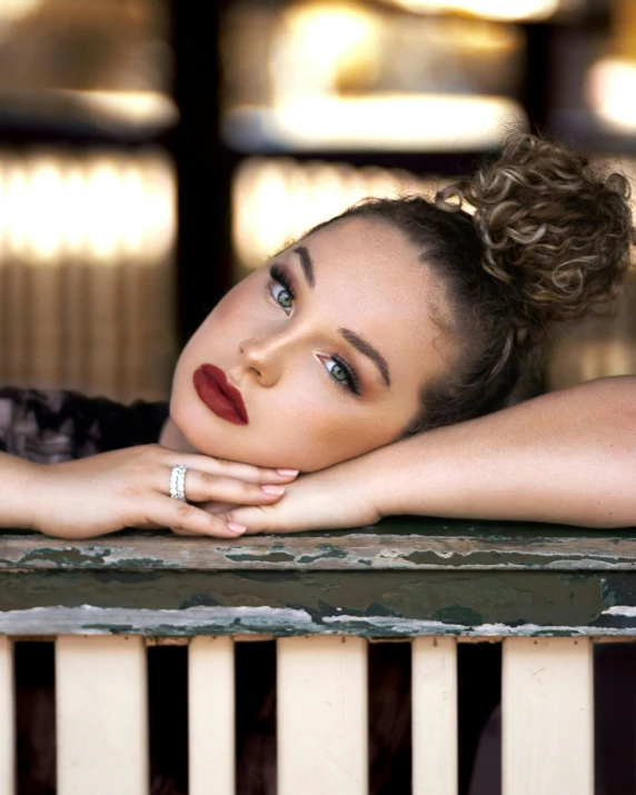 a beautiful woman laying on top of a wooden bench, an album cover, by Arabella Rankin, trending on pexels, renaissance, curly messy high bun hairstyle, portrait sophie mudd, dark lipstick, lgbtq