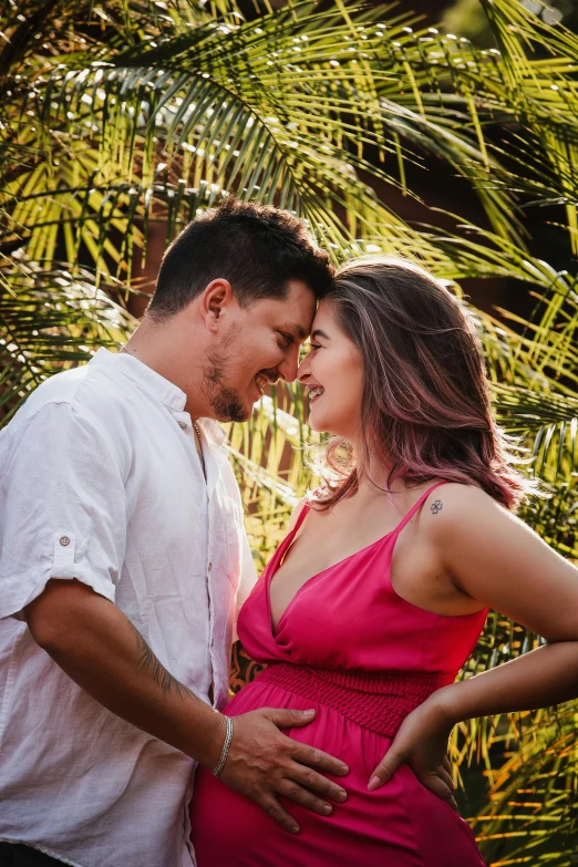 a woman in a pink dress standing next to a man in a white shirt, pexels contest winner, palm trees in the background, maternity feeling, profile image, brazilian