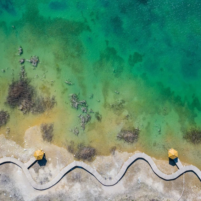 a couple of yellow umbrellas sitting on top of a sandy beach, unsplash contest winner, land art, looking down from above, green waters, the face emerges from pamukkale, near a jetty