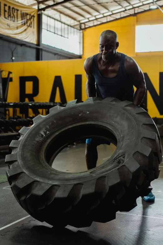 a man holding a large tire in a gym, pexels contest winner, process art, black man, yellow charcoal, pulling the move'derp banshee ', man engine