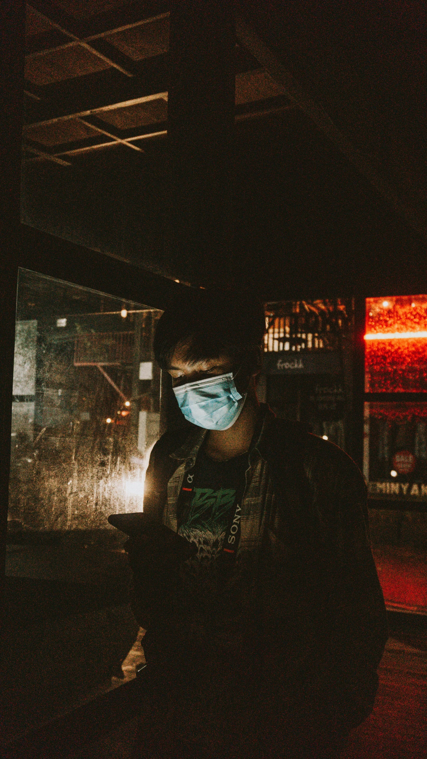 a person wearing a face mask in the dark, an album cover, inspired by Liam Wong, pexels, industrial party, looking at his phone, wearing transparent glass mask, people at work