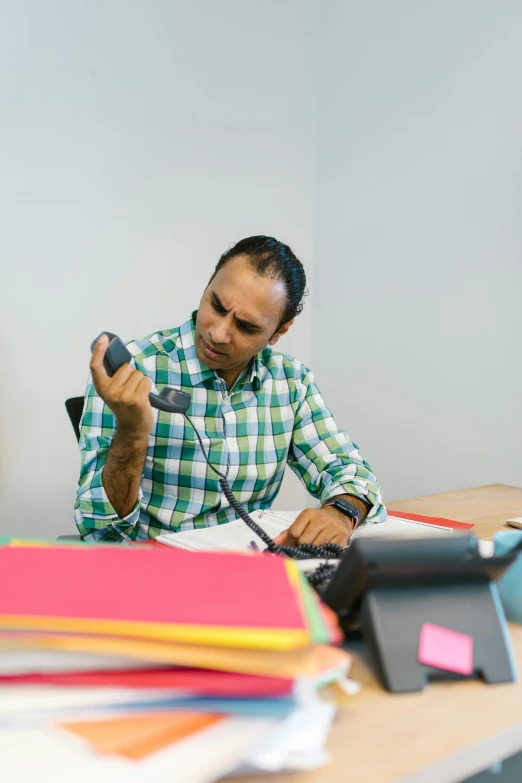 a man sitting at a desk talking on a phone, nivanh chanthara, profile image, multiple stories, colour photograph