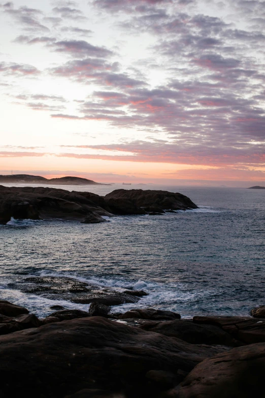 a man standing on top of a rock next to the ocean, inspired by Wilhelm Marstrand, twilight ; wide shot, pink hues, hestiasula head, panoramic shot