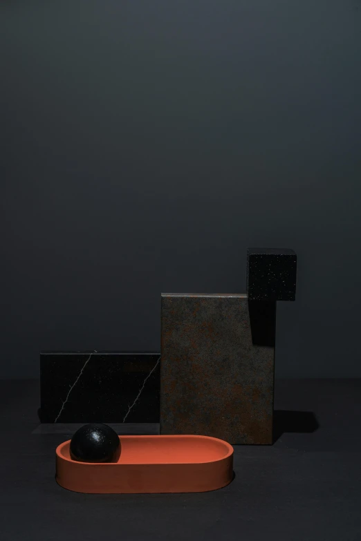 a black object sitting on top of a table, a still life, by Harvey Quaytman, unsplash, de stijl, colored marble, dark orange, sydney hanson, dwell