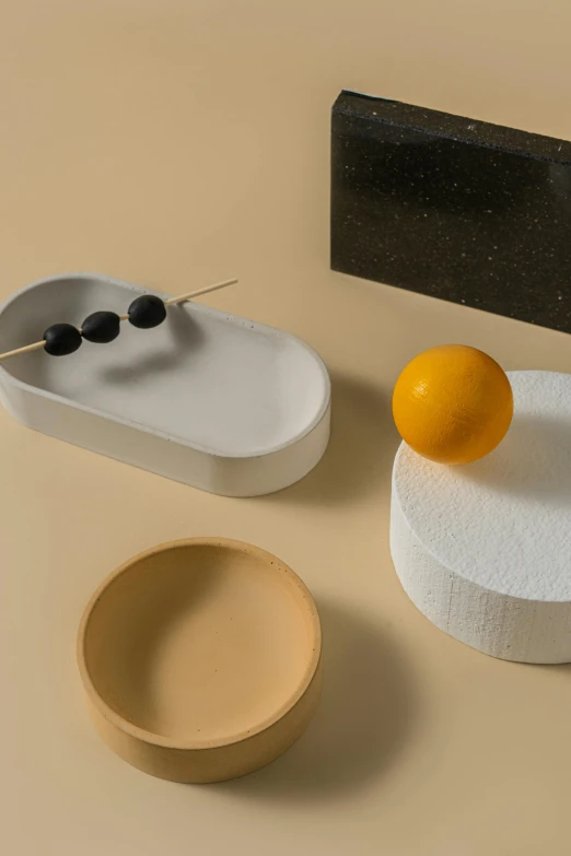 a couple of bowls sitting on top of a table, a still life, inspired by Bauhaus, minimalism, soft white rubber, snacks, lemon, random circular platforms