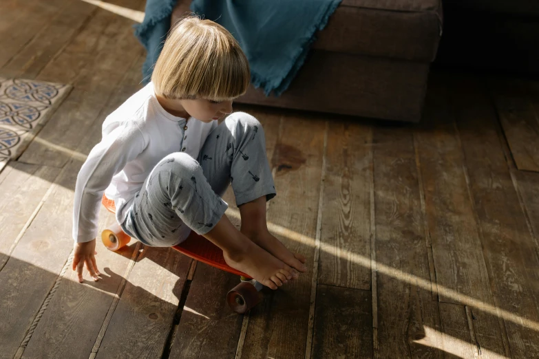 a young boy riding a skateboard on a wooden floor, by Nick Fudge, pexels contest winner, wearing pajamas, sun dappled, sittin, textured