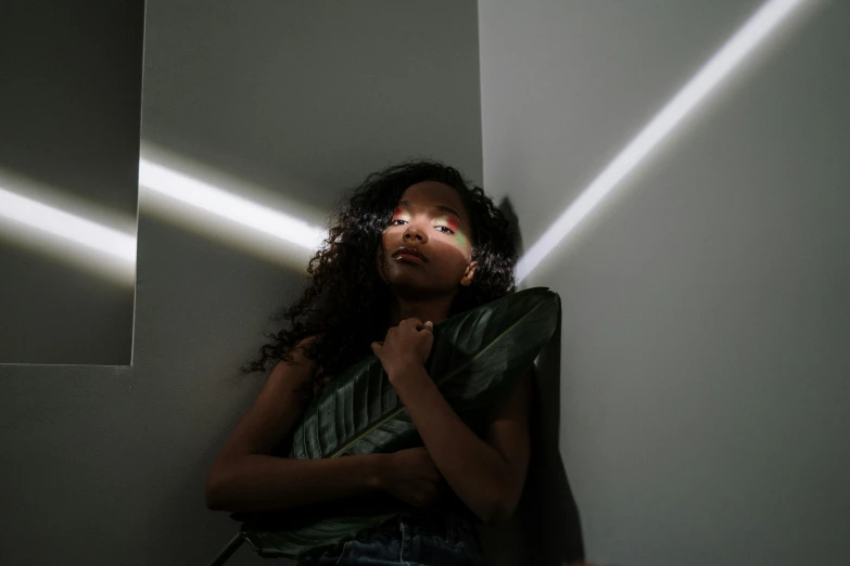 a woman leaning against a wall in a dark room, pexels contest winner, light and space, black teenage girl, light beam, with brown skin, bella poarch