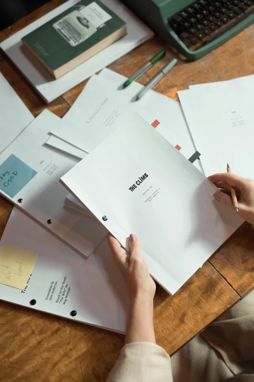 a person sitting at a desk with papers and a laptop, unsplash, movie cover, character sheets on table, holding a stack of books, production photo