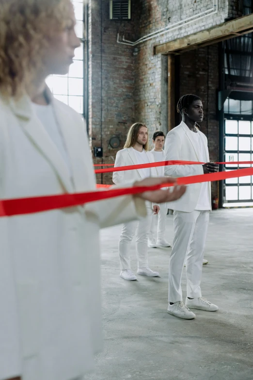 a group of people standing around a red ribbon, inspired by Vanessa Beecroft, visual art, wearing white suit, in a warehouse, hammershøi, olympics ceremony