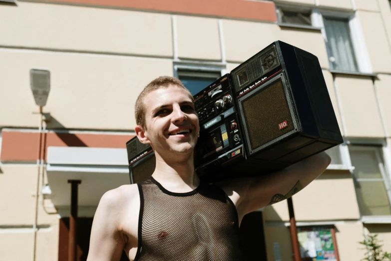 a man holding a radio in front of a building, by Attila Meszlenyi, reddit, no shirt under the vest, big ghetto blaster, vitalik buterin, huge earrings and queer make up