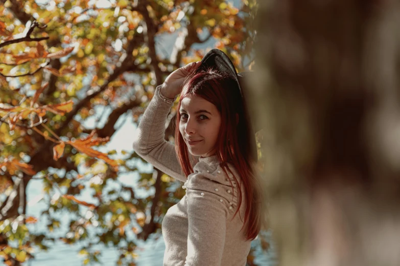 a woman with red hair standing in front of a tree, pexels contest winner, pokimane, wearing a white sweater, avatar image, autumn bokeh