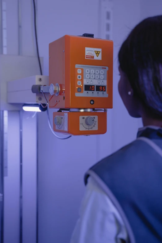 a woman standing in front of a machine, orange glow, on a advanced lab, afro tech, colour photograph