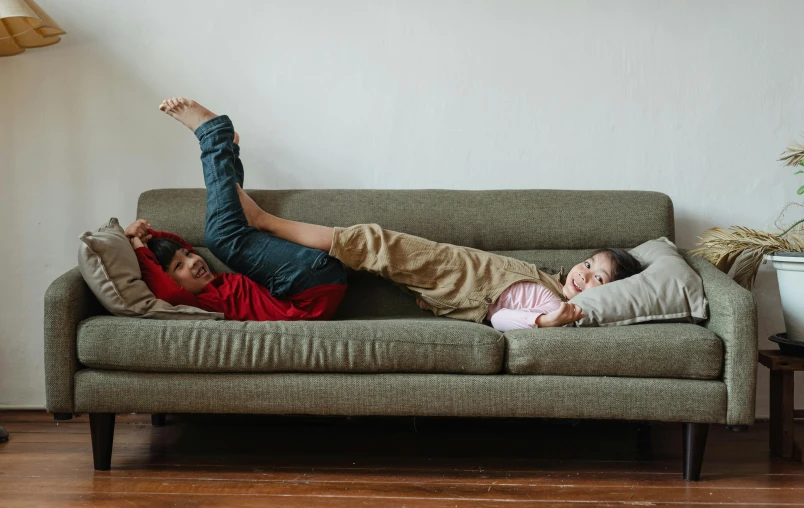 a couple of people laying on top of a couch, by Carey Morris, pexels contest winner, kids playing, asian female, unique design, unbeatable quality