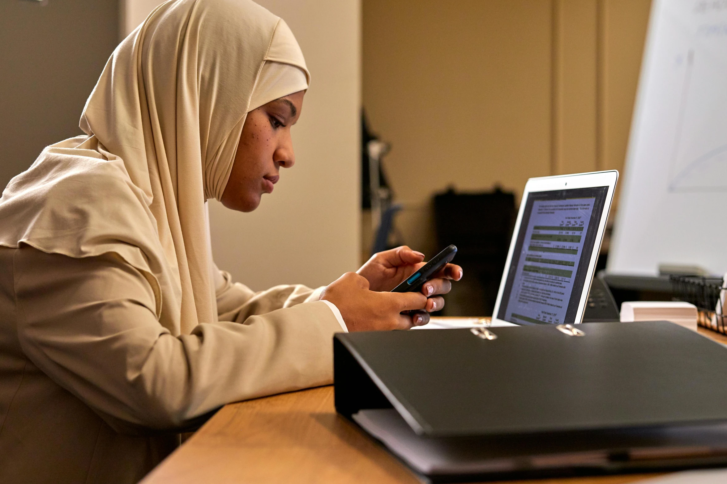 a woman sitting at a table with a laptop and cell phone, hurufiyya, learning, thumbnail, ameera al-taweel, medium level shot