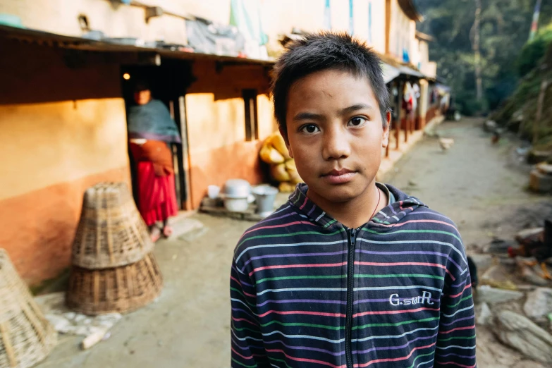 a young boy standing in front of a building, a portrait, pexels contest winner, hurufiyya, nepal, tommy 1 6 years old, in a village street, sydney hanson