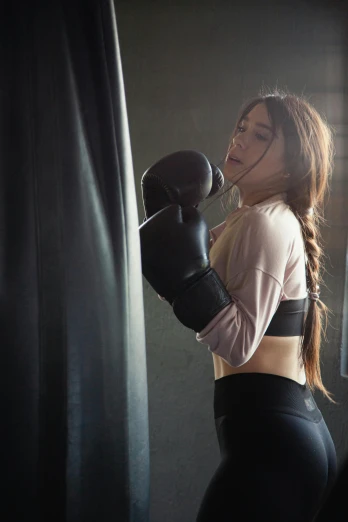 a woman standing next to a punching bag, by Arabella Rankin, pexels contest winner, hailee steinfeld, woman with braided brown hair, profile image, in a fighting pose