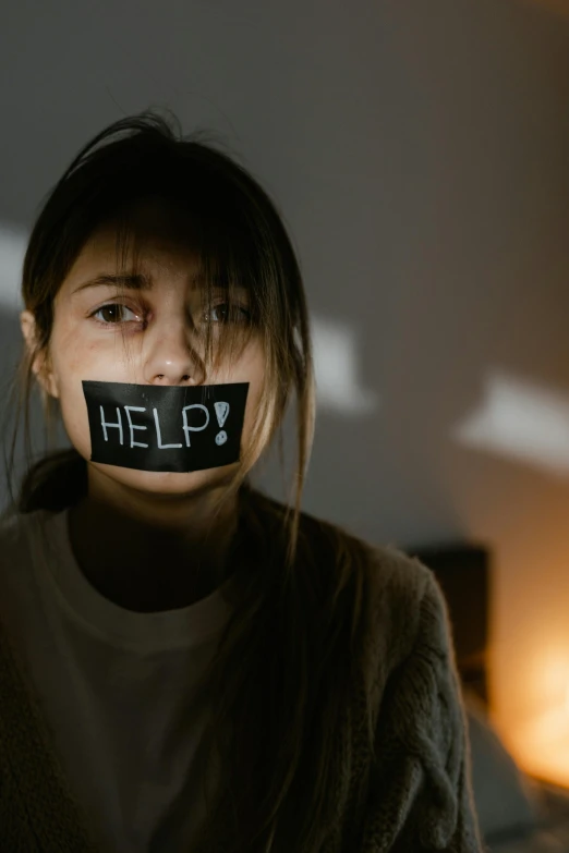 a woman with a tape over her mouth, a picture, trending on pexels, woman holding sign, help, dimly lit, clinically depressed