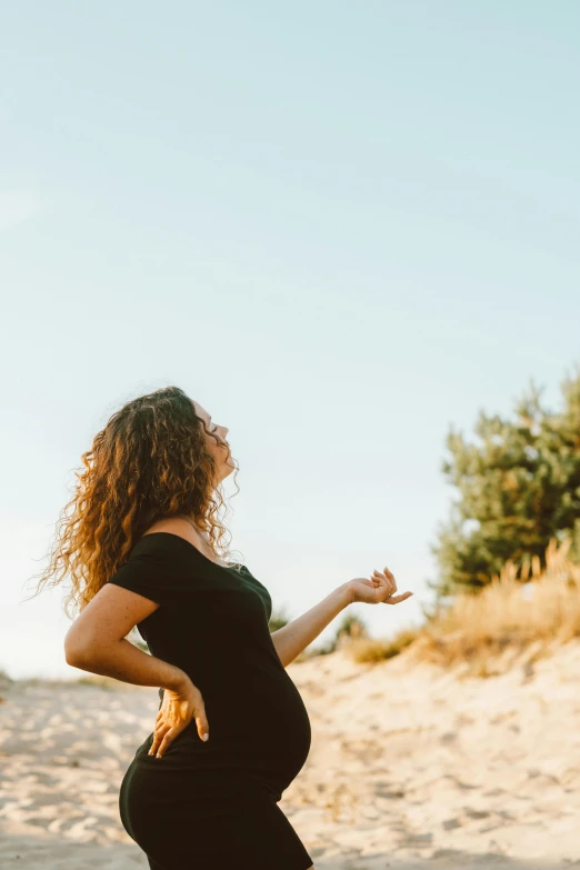 a pregnant woman standing on top of a sandy beach, pexels contest winner, renaissance, shrugging arms, curly haired, profile image, in sunny weather