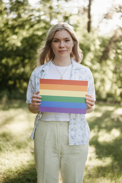 a woman standing in a field holding a rainbow sign, trending on pexels, a handsome, wearing stripe shirt, a wooden, lesbian