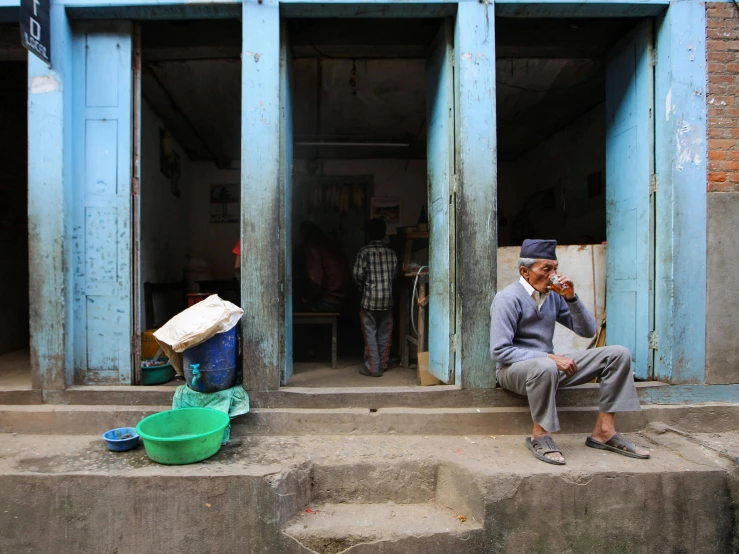 a man sitting on the steps of a building, by Peter Churcher, pexels contest winner, bengal school of art, stood outside a corner shop, thumbnail, slide show, drinking