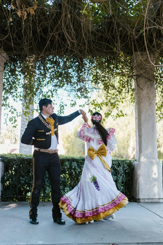 a man standing next to a woman in a white dress, inspired by Germán Londoño, folklorico, prima ballerina in rose garden, with yellow flowers around it, full dress uniform