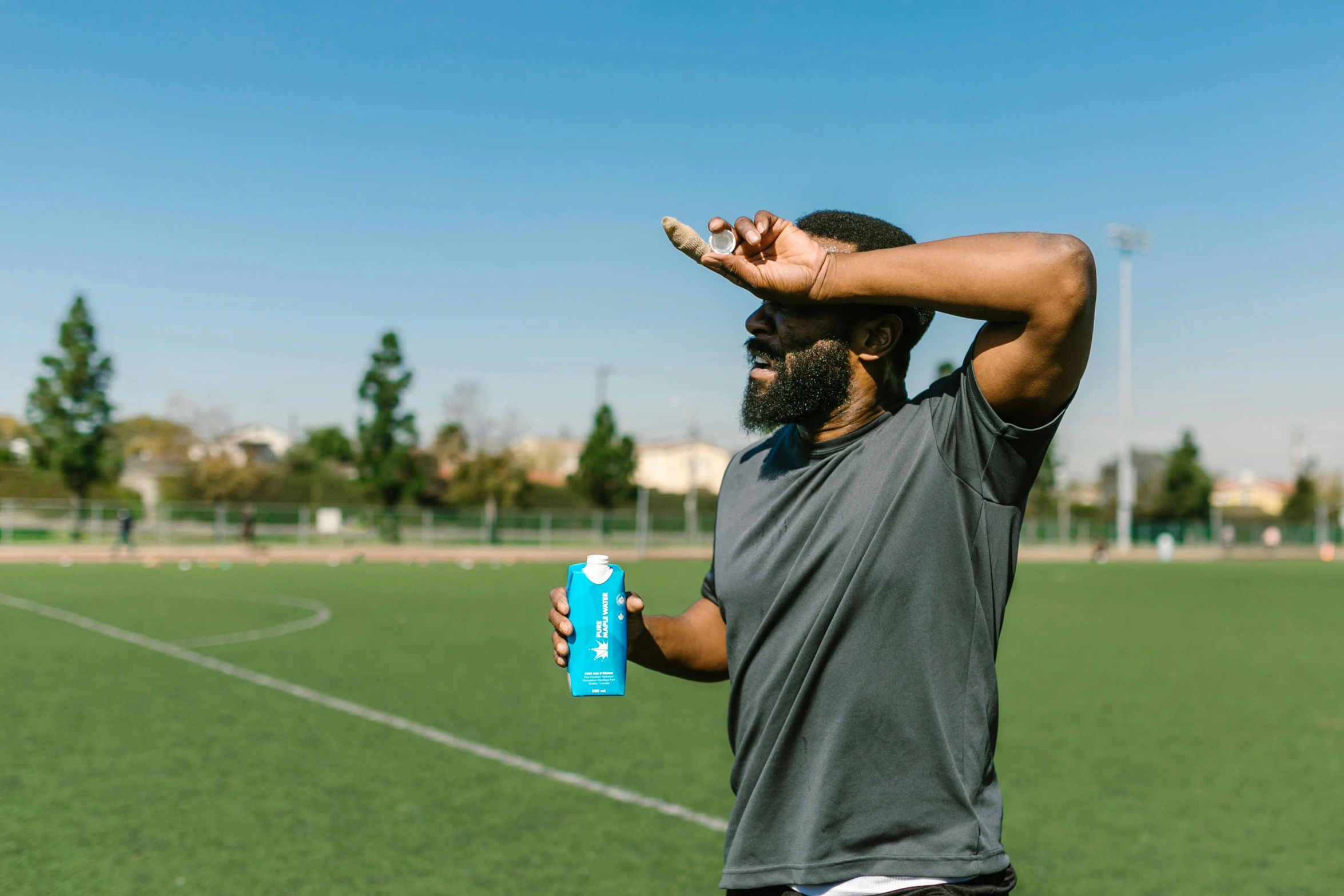 a man standing on a soccer field holding a water bottle, happening, teal energy, photoshoot for skincare brand, rave otufit, man is with black skin