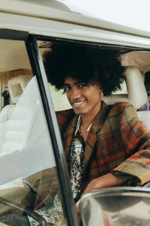 a woman sitting in the driver's seat of a car, by Winona Nelson, pexels contest winner, afrofuturism, dressed in 1970s menswear, tartan garment, imaan hammam, smiling fashion model